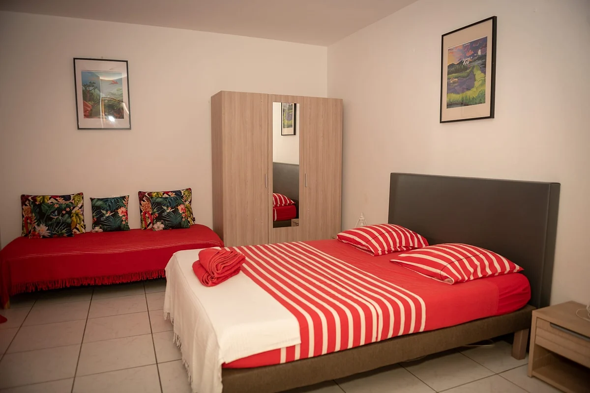 La chambre Hibiscus, son grand lit au linge rayé rouge et blanc et sa banquette