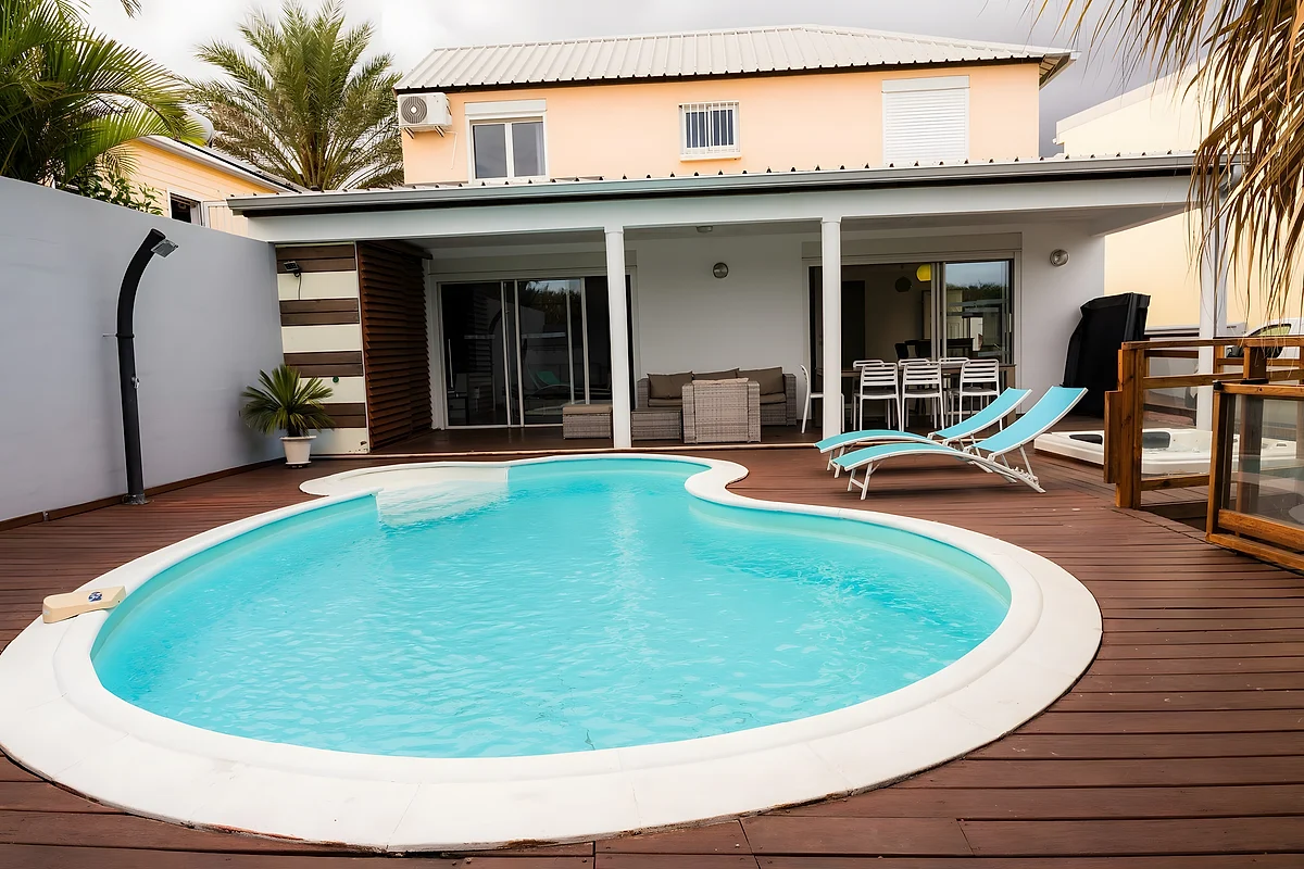 La piscine de la villa, sa terrasse en bois et la maison sous les palmiers